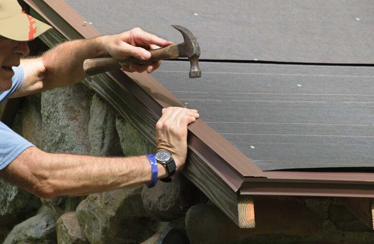 A person using a roof rake to clear snow from the edge of a residential roof in winter.